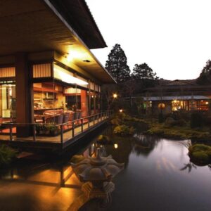 Lit wooden veranda overlooking reflecting pond and stone lanterns in a garden at dusk, Yoshimatsu Kanagawa