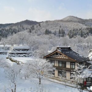 Traditional wooden ryokan buildings surrounded by snow with forested hills at Yukaen, Iwate Tōhoku