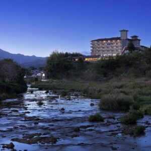 Multi-story ryokan building illuminated beside a rocky river with mountains in the background at dusk