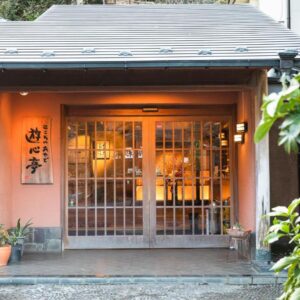 Traditional wooden entrance with lattice doors, potted plants and kanji sign at Yushintei ryokan in Kanagawa