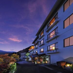 Dusk exterior of multi-story ryokan with illuminated windows and mountain backdrop in Miyagi Tōhoku