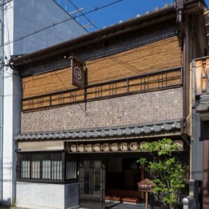 Two-story wooden ryokan facade with bamboo blinds, tiled roof and lantern-decorated entrance at Dozen-Ryokan Kyoto