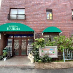 Street-level brick facade with green awnings and potted plants at Business Inn Haijima entrance in Tokyo, Kantō