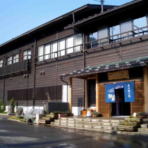 Wooden two-story ryokan exterior with blue noren and stone steps, Shirakawagō no Yu, Gifu