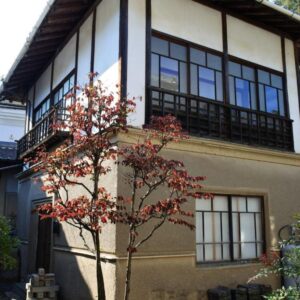 Two-story traditional Japanese ryokan exterior with wooden framed windows and a small red-leaved tree at Yamashiroya Resort Nagano