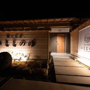 Warm lit wooden entrance with stone path and noren curtain at Yudono Totonoyu, Yokokawa Onsen, Shizuoka