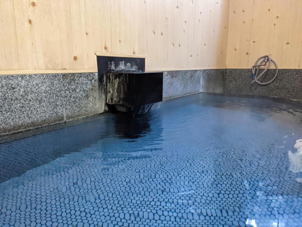 Wooden Indoor Onsen Bath at Onsenya Hirosuke Fukushima Indoor onsen bath with wooden spout, tiled floor and stone edging at Onsenya Hirosuke, Fukushima