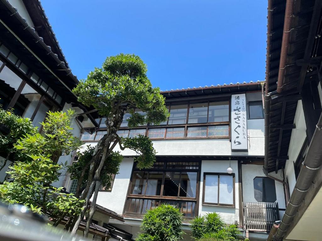 Ryokan exterior at Yuyado Sasakura Hyōgo Traditional multi-story ryokan exterior with wooden balconies, shoji windows and courtyard tree at Yuyado Sasakura, Hyōgo