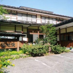 Two-story traditional ryokan facade with wooden entrance, signboard and surrounding greenery at Yushō Fukujikan, Gifu