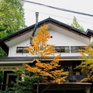Two-story ryokan facade with orange autumn leaves at Okara Sansō in Nagano, Chūbu region